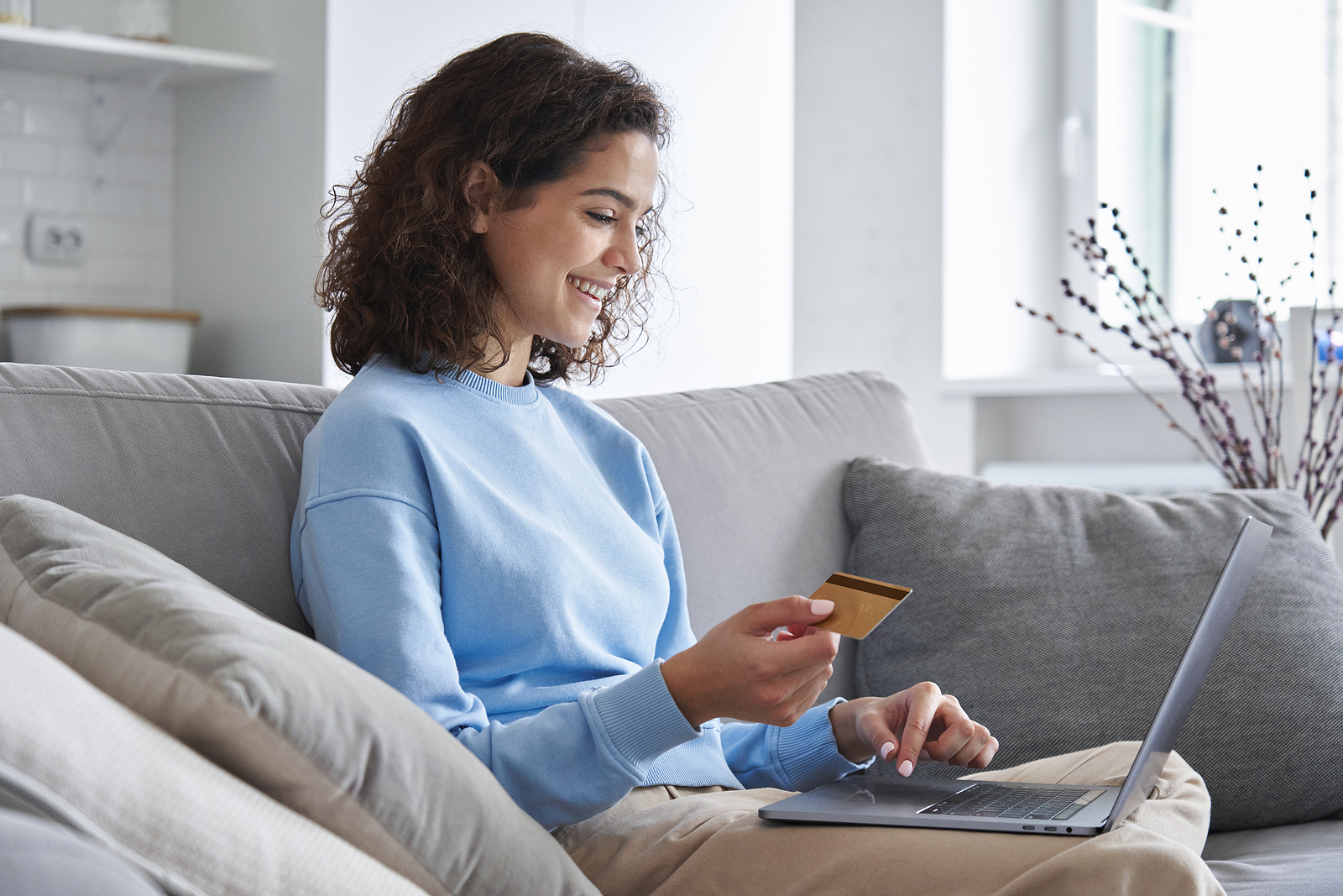 Happy hispanic young woman consumer holding credit card and laptop buying online at home. Female shopper customer shopping on ecommerce website market place making digital payment using bonus money.